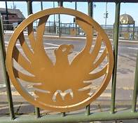 A gold emblem of a phoenix on a green metal fence