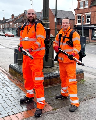 Two men in hi vis with back pack machines and holding suction tubes.