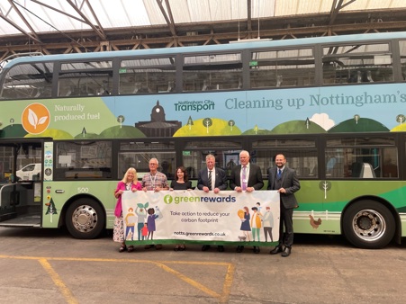 Group of people holding Green Rewards banner saying: Taking action to reduce your carbon footprint. Stood in front of biogas bus.