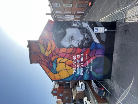 Mural with: a portrait of Lawrence on the right, a colourful stained glass window style phoenix on the left. Quote that reads: The living moment is everything, with Lawrence's signature and the dates 1885 - 1930.