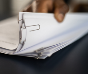 Pile of documents held together with paperclips with a hand holding them