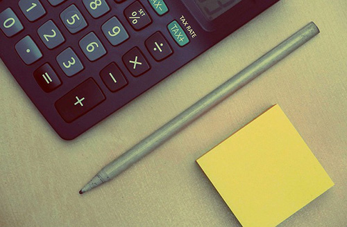 A calculator, pencil, and some post-it notes on a table