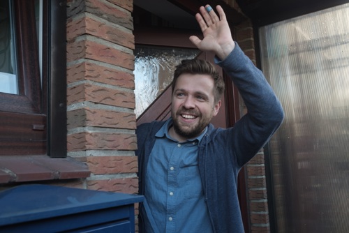man waving outside his front door