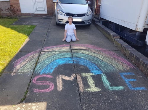 young boy say outside with his rainbow drawing