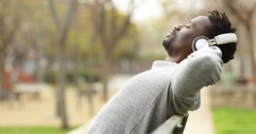 man relaxing on a park bench listening to music through his headphones