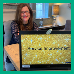 Nicky sitting behind laptop - laptop screen say 'service improvement' award