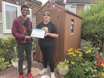 2 people smiling in front of shed